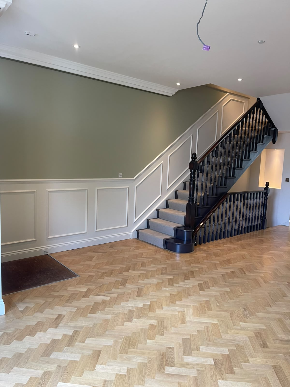 Sage green hallway with white wainscoting and freshly painted dark staircase