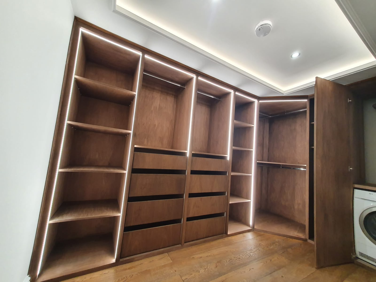 Fitted dark wood wardrobe with hanging rails, drawers and integrated lighting