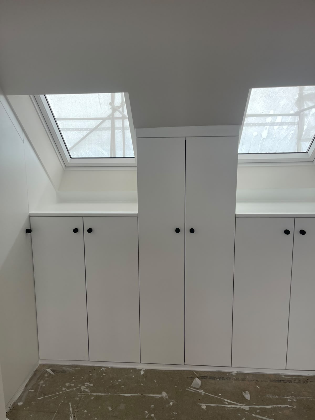 Finished white fitted wardrobes with black knobs built into a sloped attic ceiling between skylights