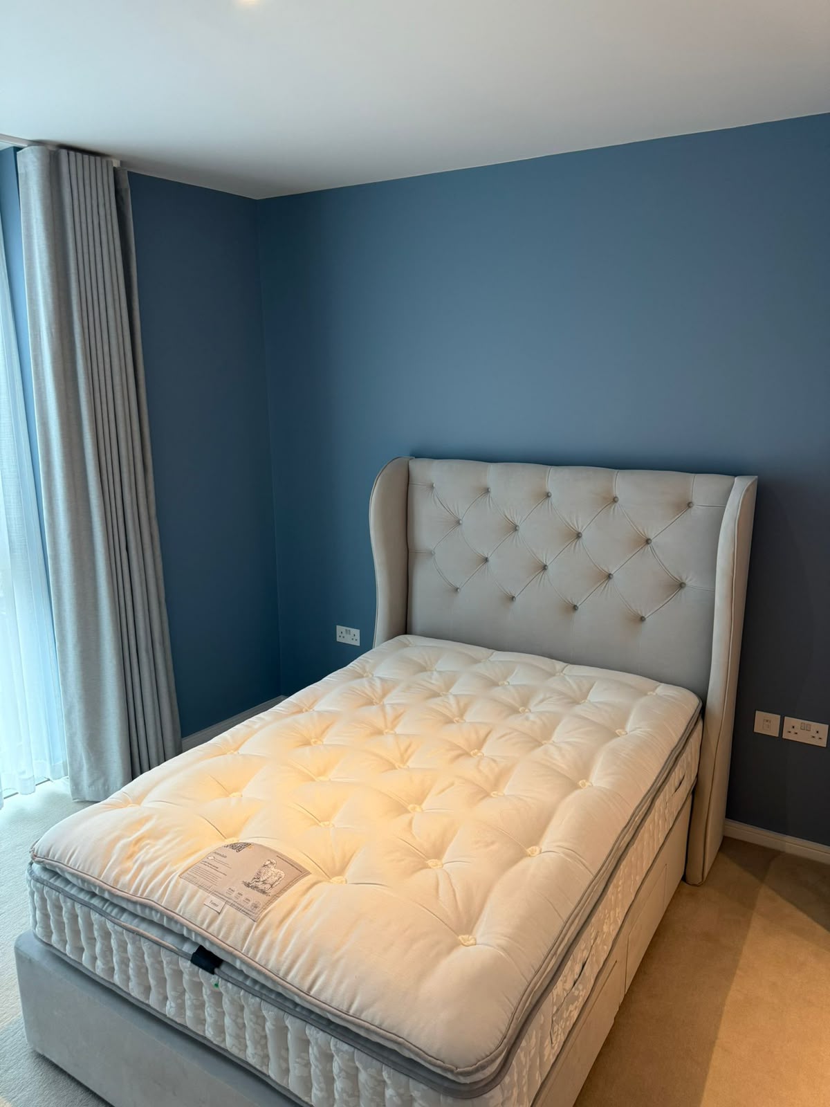 Bedroom with a light blue feature wall behind a tufted headboard
