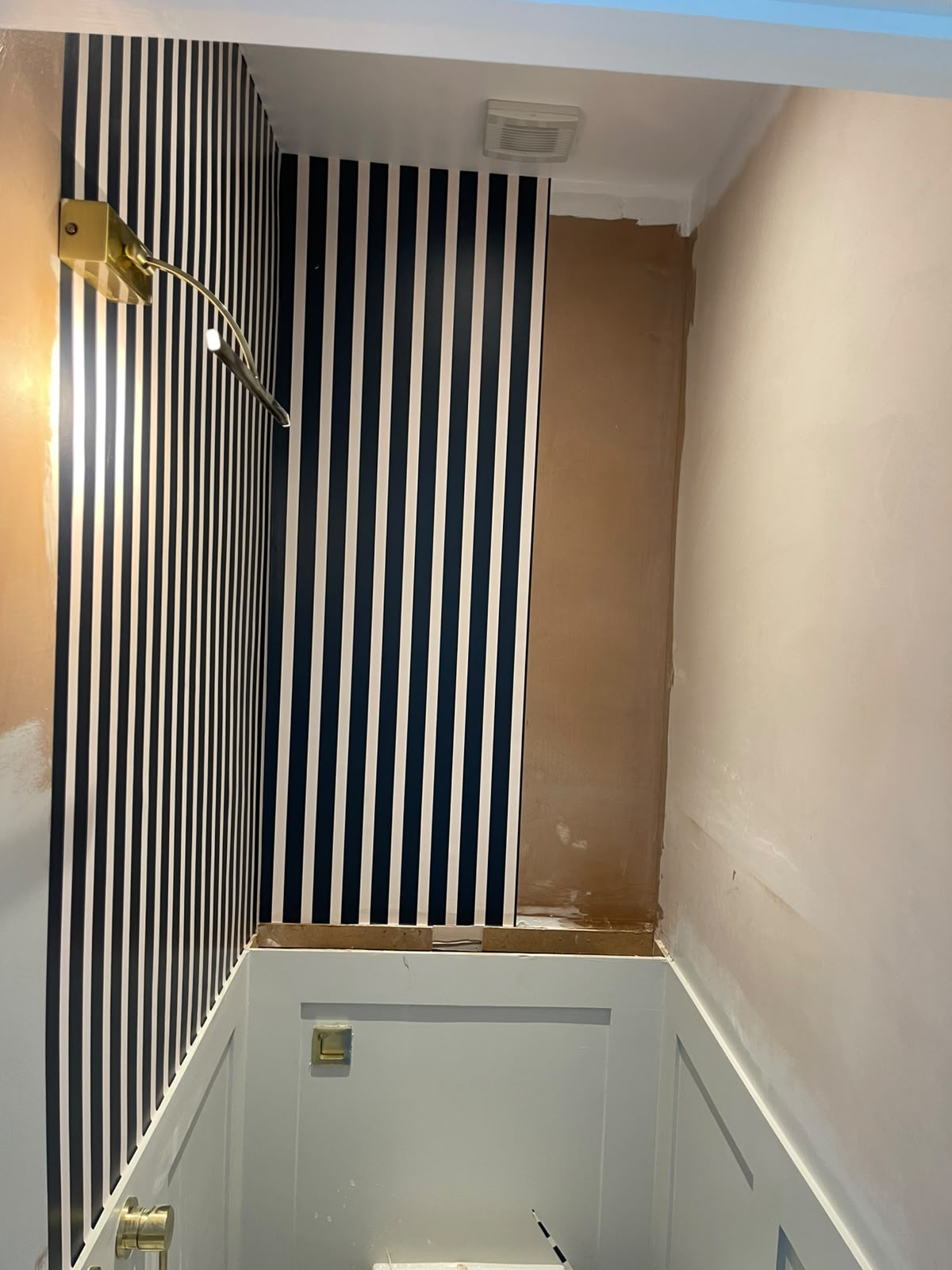Navy and white striped wallpaper installation in progress on a stairwell landing