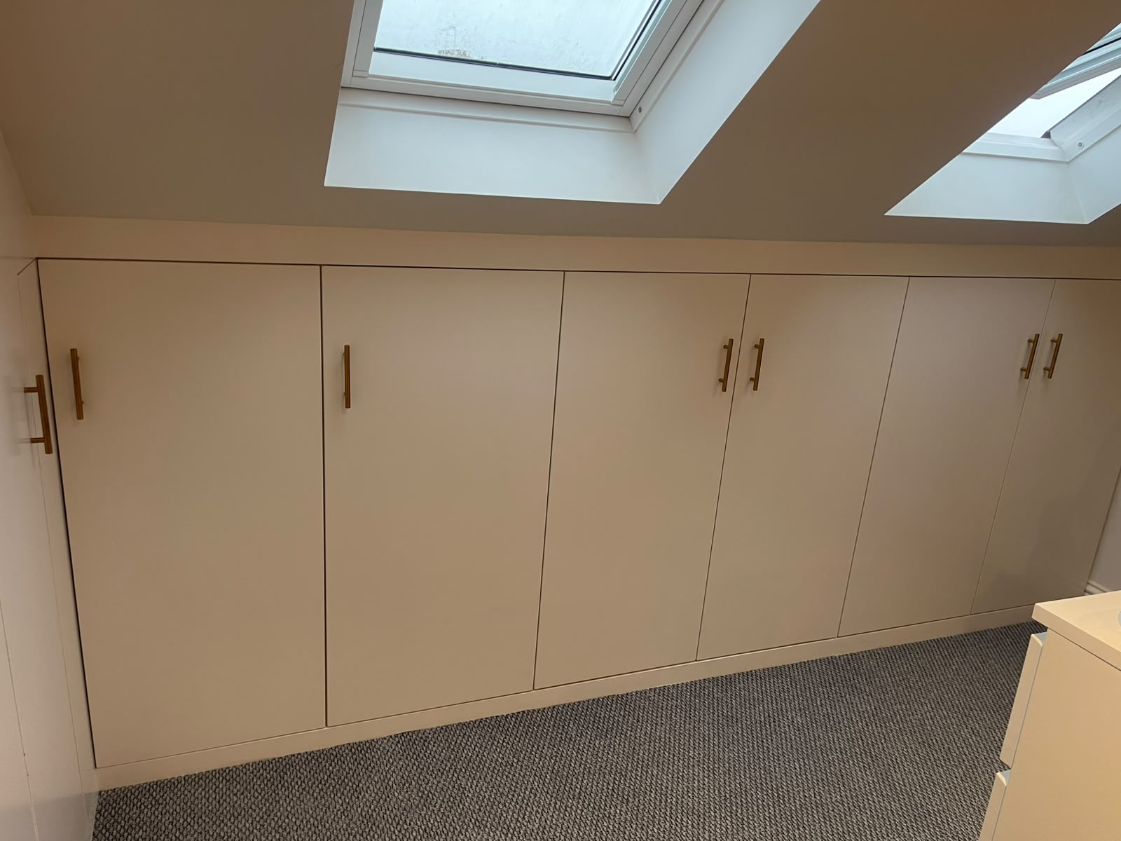 Low white fitted cabinets along a sloped attic wall under skylights