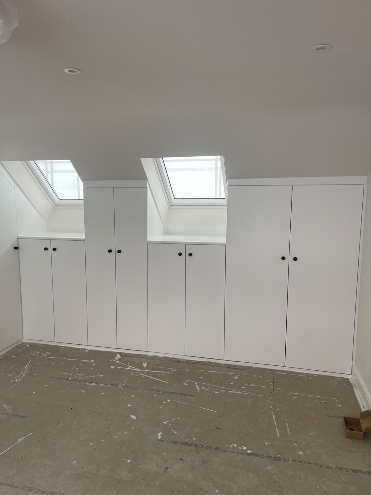 White fitted wardrobe installation built around attic skylights with dark handles