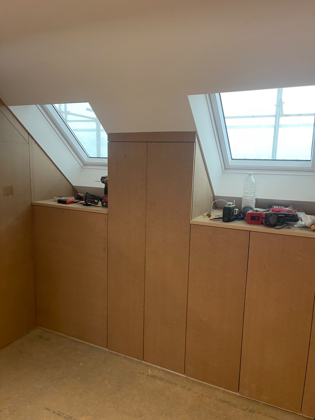 Raw MDF fitted wardrobe carcass built into a sloped attic wall between two skylights