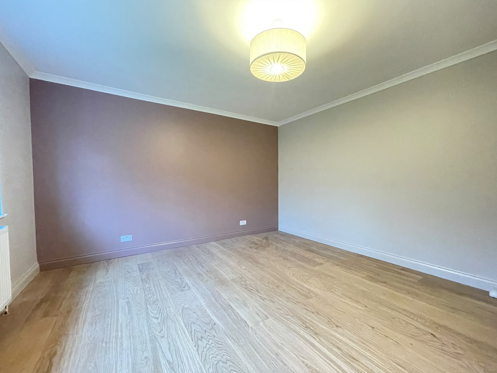 Bedroom with a soft mauve accent wall and light wood flooring