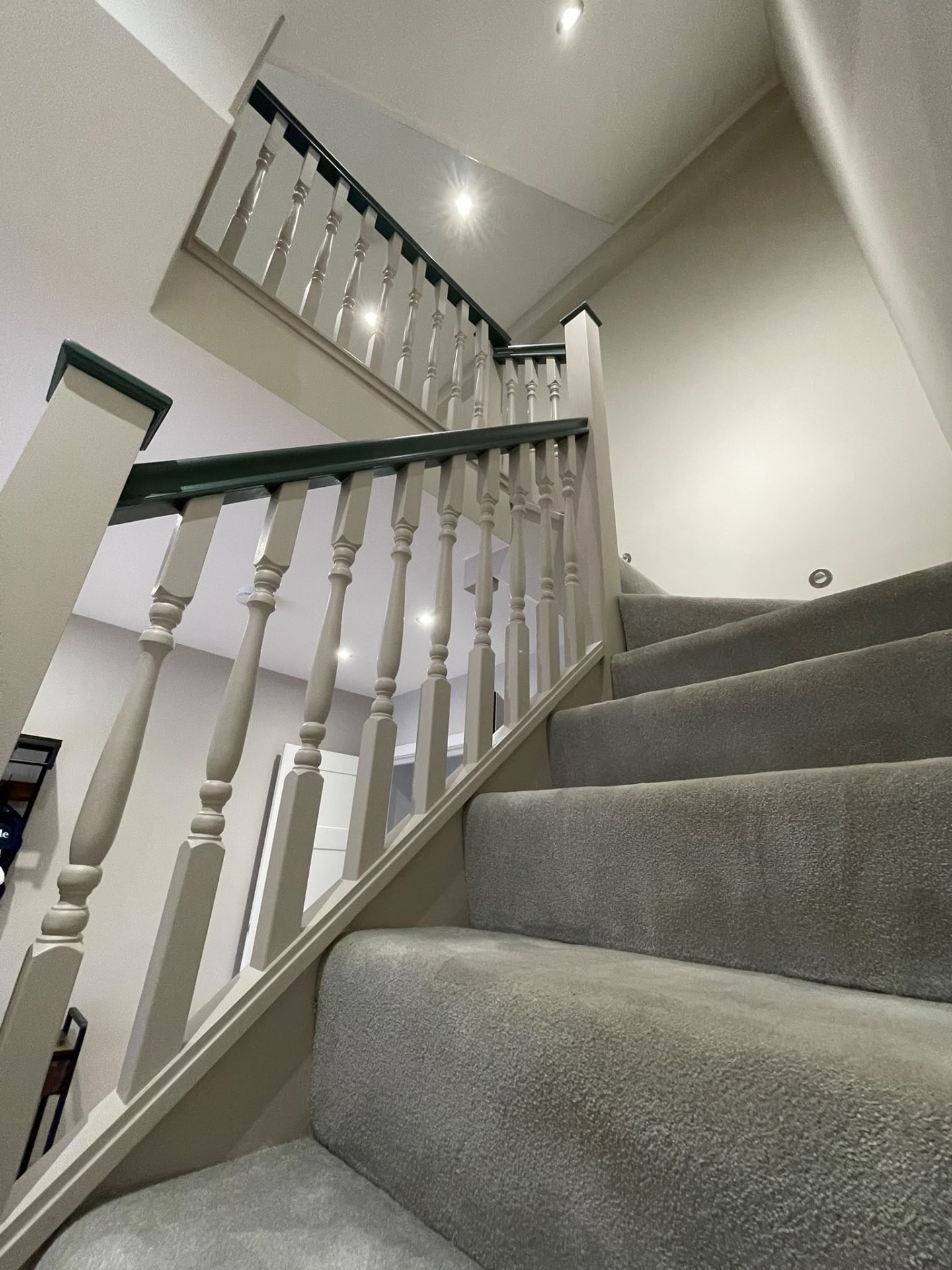 Painted staircase viewed from the steps with finished spindles, walls and dark green handrail