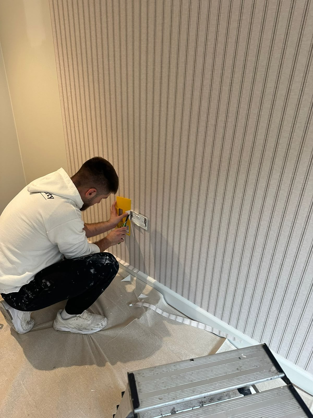 Neutral ticking-stripe wallpaper hung around a socket with precise cuts