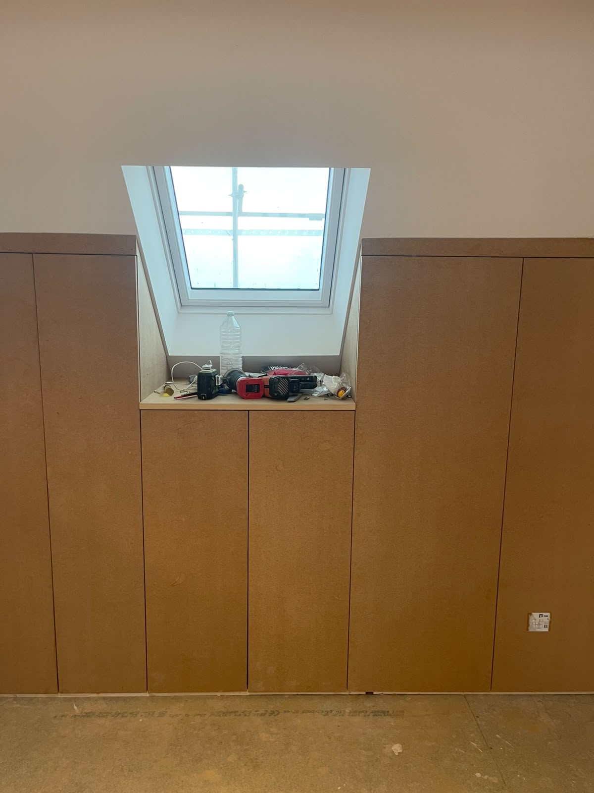 Raw MDF fitted wardrobes flanking a skylight beneath a sloped attic ceiling