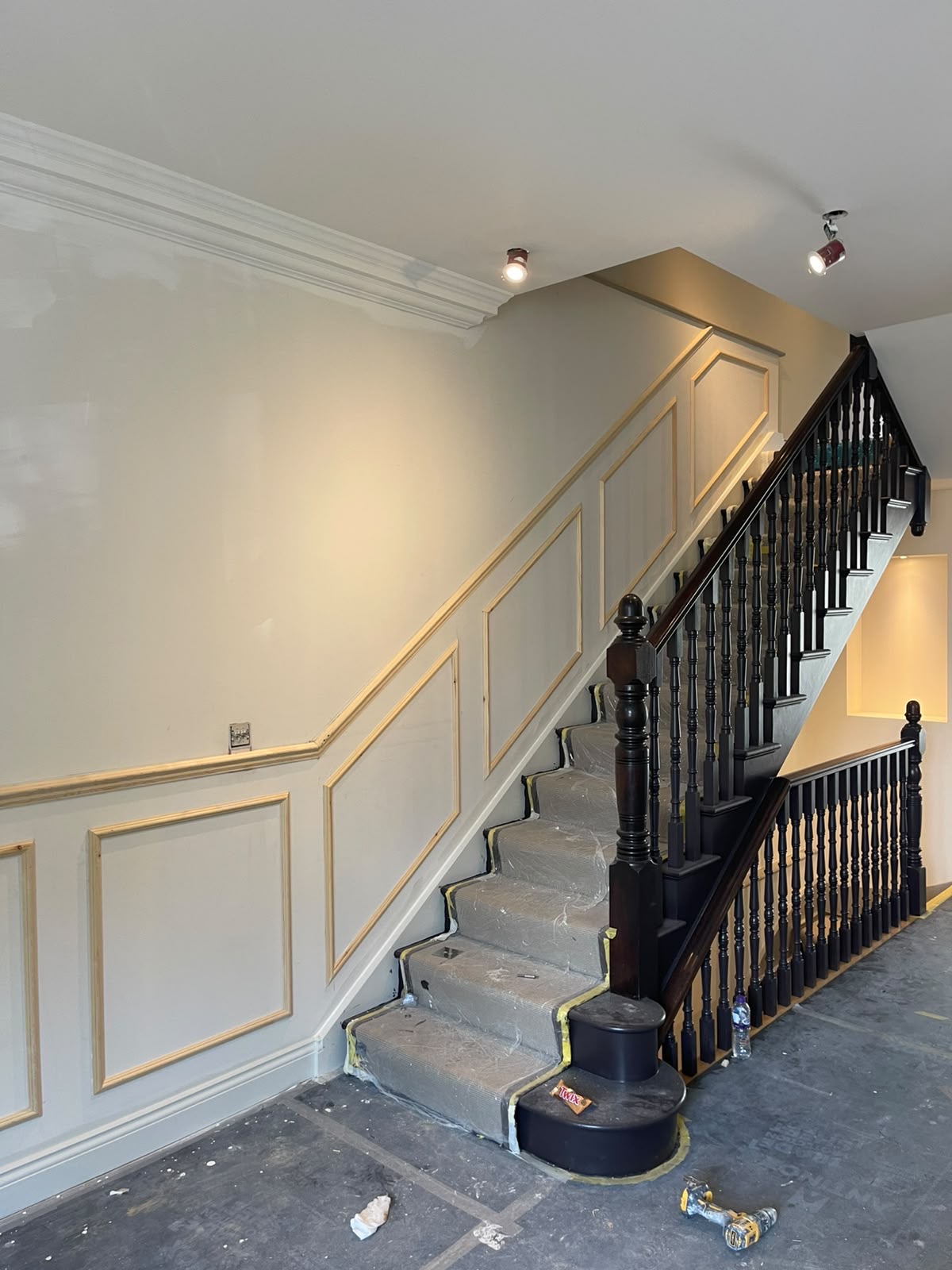 Before: unfinished staircase with protected treads, exposed timber panelling and drill on the floor