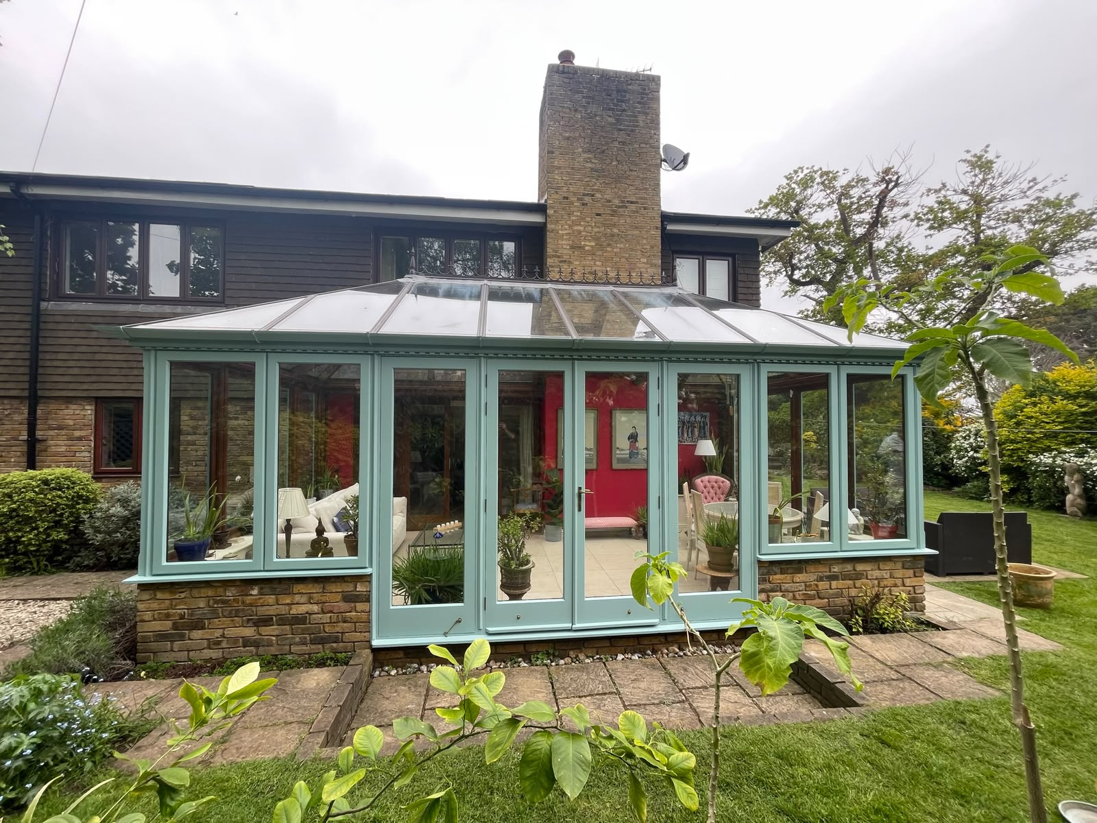 Duck-egg painted conservatory with glazed roof against a brick period home