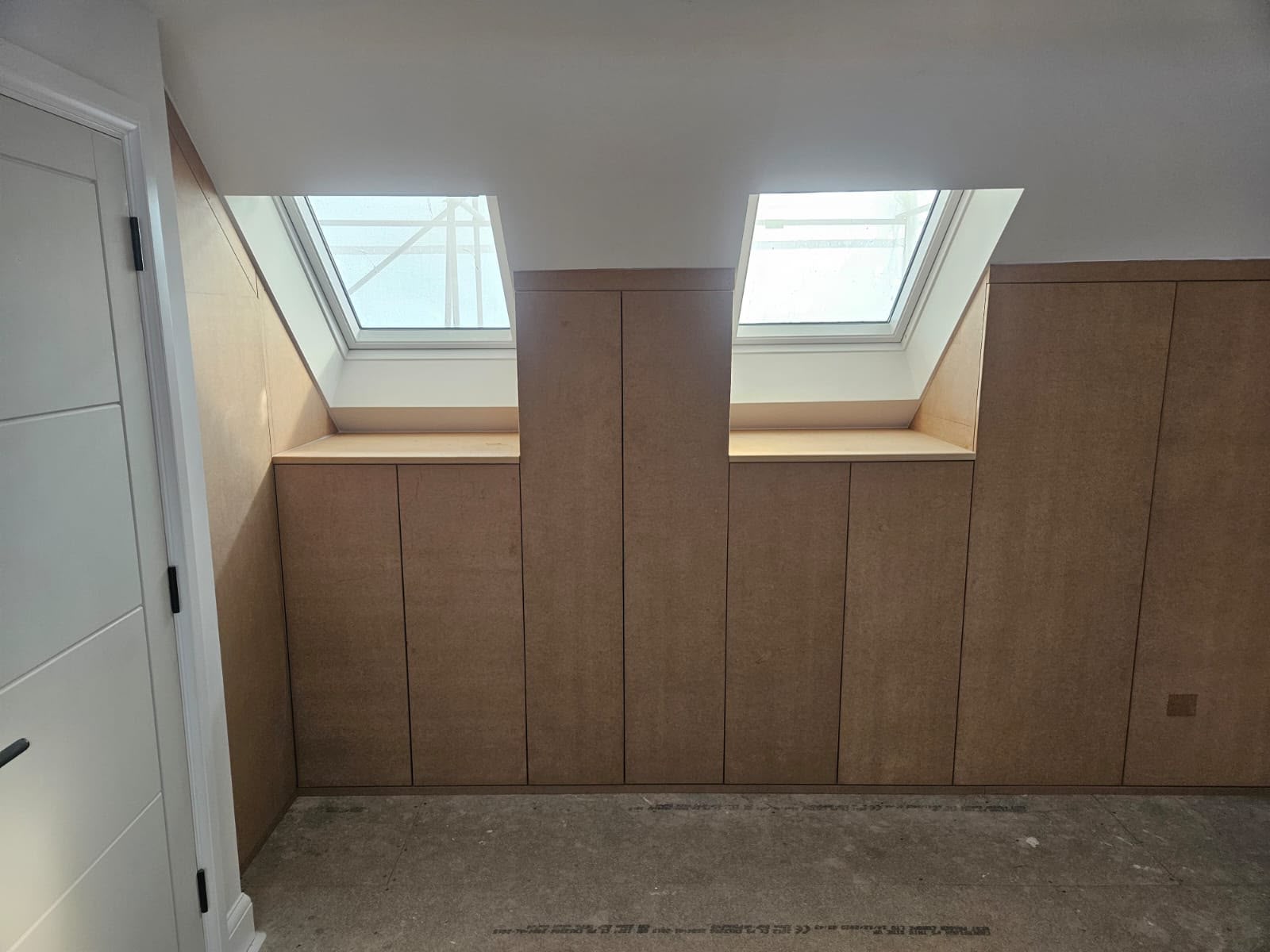 Light timber fitted wardrobes built into a sloped attic wall beneath two skylights
