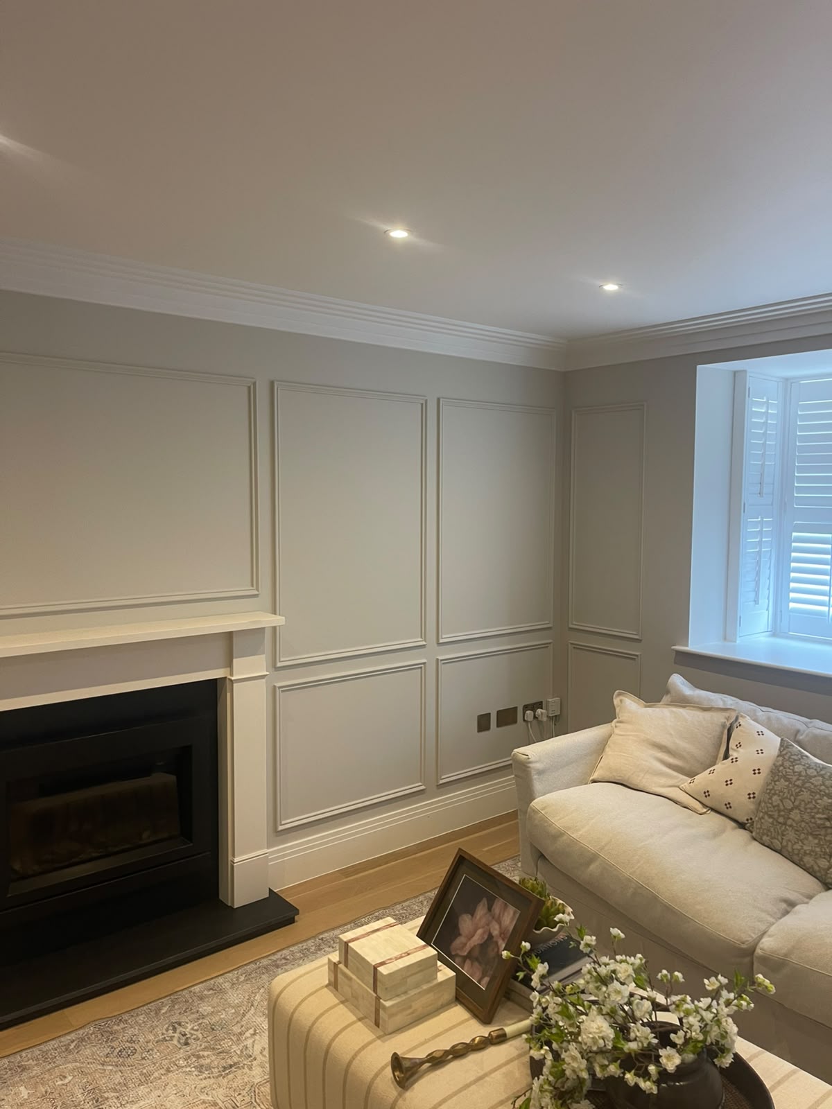 Finished wall panelling between a fireplace and a shuttered living room window